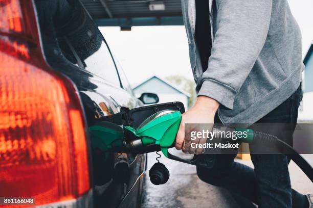 midsection of man refueling car at gas station - zapfsäule stock-fotos und bilder