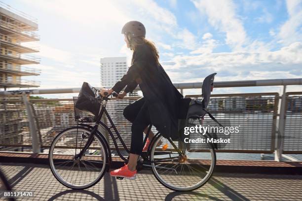 side view of mature woman cycling on footbridge against sky - bicycle safety light stockfoto's en -beelden