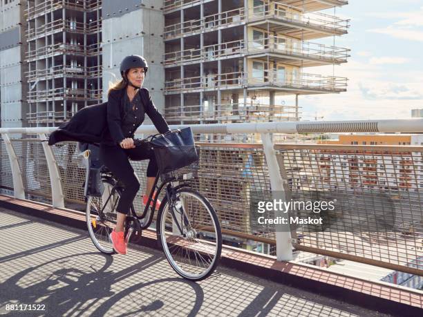 mature woman cycling on footbridge against building - urban bicycle stock pictures, royalty-free photos & images
