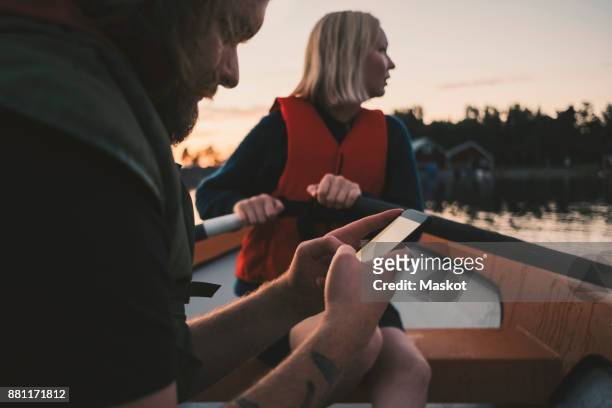 man using mobile phone while woman rowing boat on lake - boat scandinavia stock pictures, royalty-free photos & images