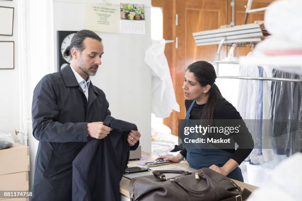 mature male owner showing suit to female entrepreneur at laundromat - dry cleaner stock-fotos und bilder