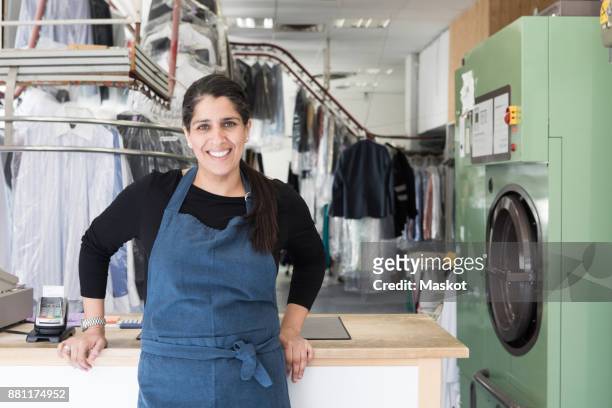 portrait of smiling mature female dry cleaner standing at laundromat - dry cleaner stock-fotos und bilder