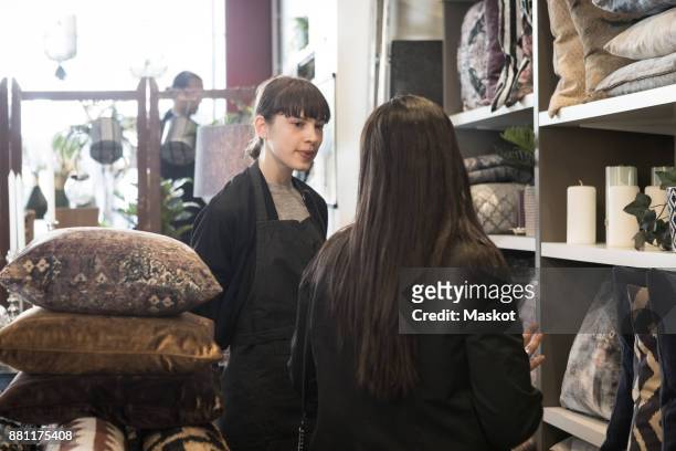 female customer talking with young owner while standing by cushions rack at store - tool rack ストックフォトと画像