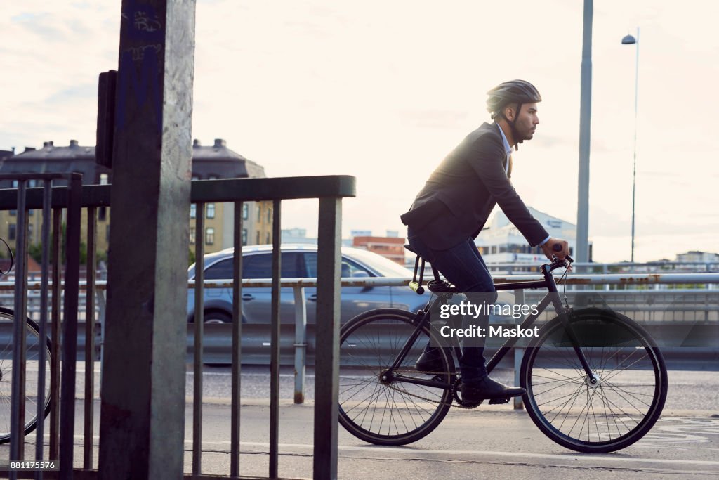 Side view of businessman cycling on street against sky