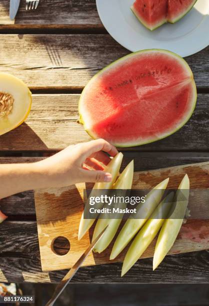 cropped image of woman slicing honeydew melon at table on sunny day - honeydew melon stock pictures, royalty-free photos & images