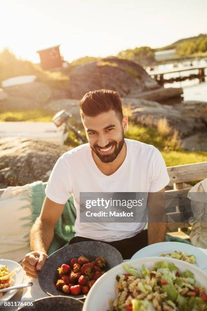 portrait of happy young man enjoying lunch at party on jetty during sunny day - sunny days foto e immagini stock