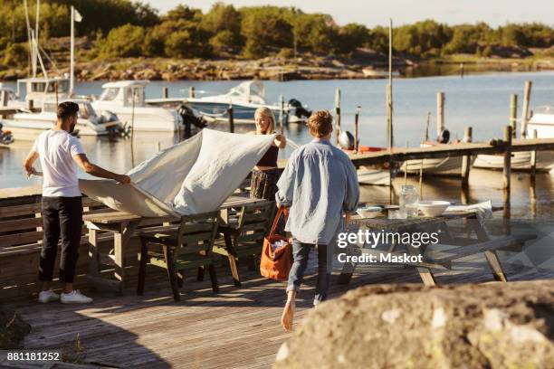 friends putting cloth on table at jetty on sunny day - scandinavia picnic stock pictures, royalty-free photos & images