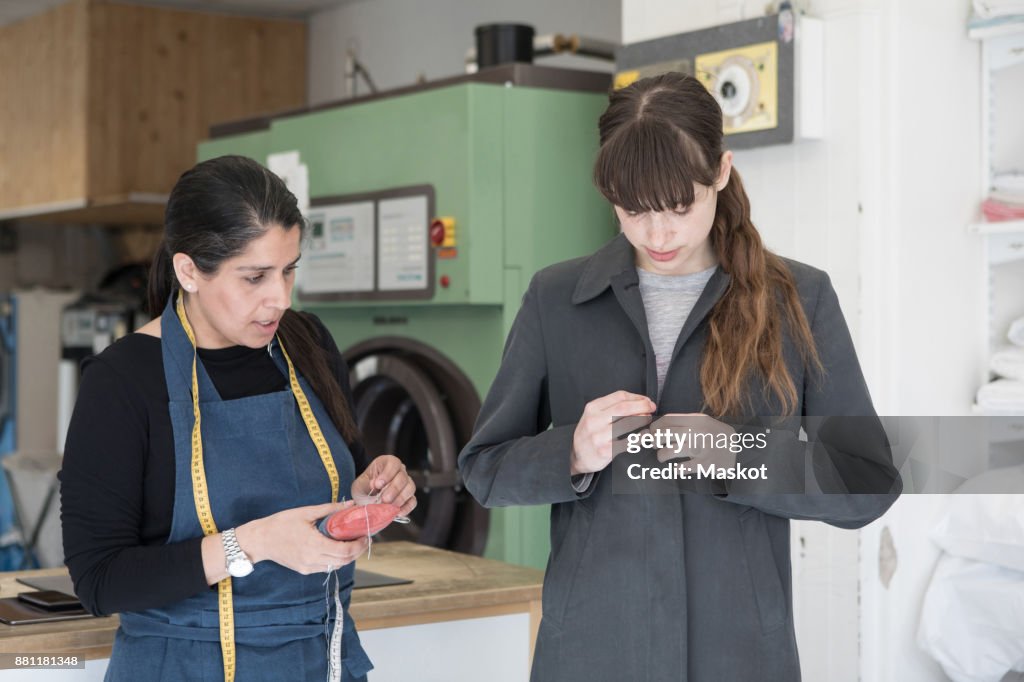 Mature female tailor standing by young customer wearing overcoat at Laundromat
