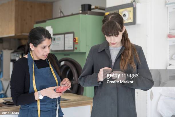 mature female tailor standing by young customer wearing overcoat at laundromat - オーバーコート ストックフォトと画像