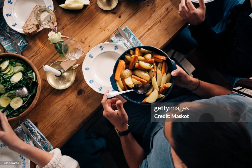 High angle view of man holding utensil of potatoes and carrots while sitting with friends