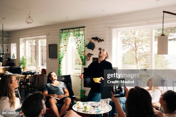 playful young man catching snack with mouth while friends watching him in cottage - catching food stock pictures, royalty-free photos & images