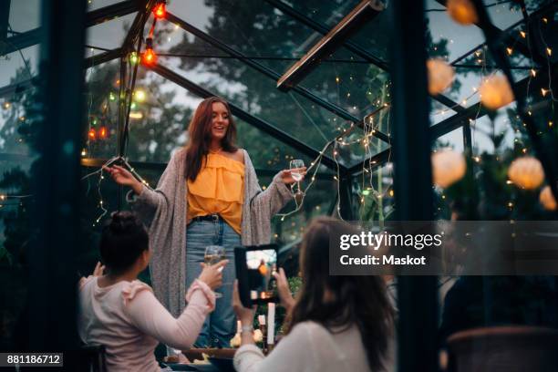 young woman standing while singing for friends in glass cabin - friendship background stock pictures, royalty-free photos & images