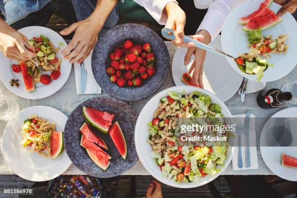 directly above shot of friends enjoying lunch at picnic table on sunny day - garden table stock-fotos und bilder
