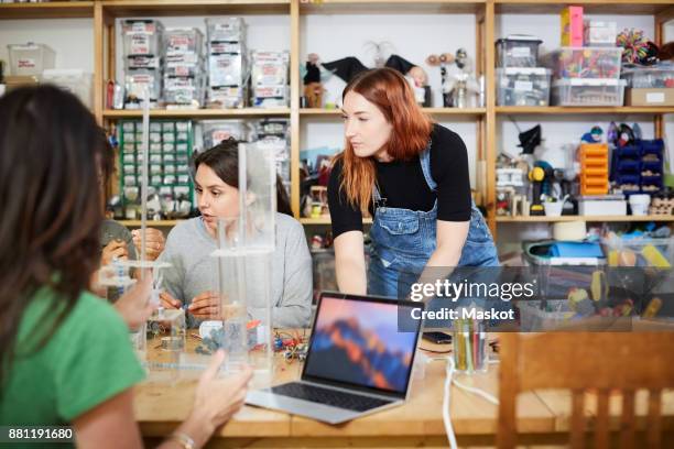 young redhead technician standing by female coworkers at workshop - inventor stock pictures, royalty-free photos & images