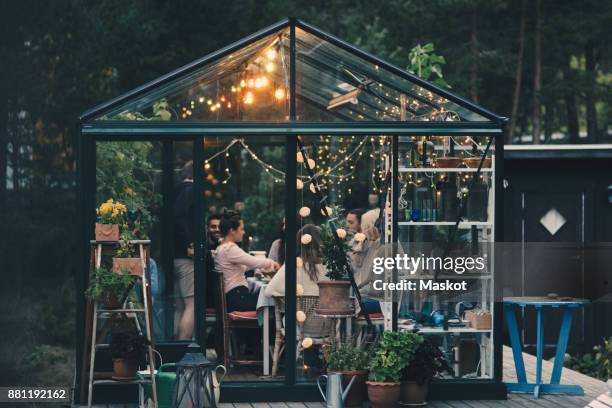 young multi-ethnic friends enjoying dinner party in glass conservatory room at back yard - garden lighting stock pictures, royalty-free photos & images