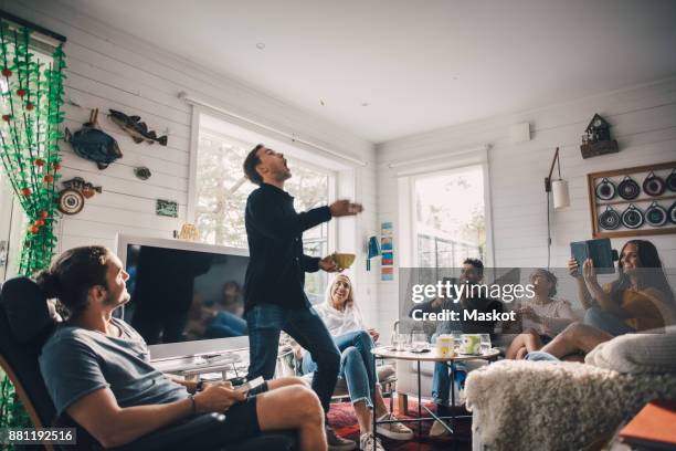 friends photographing man throwing food while standing in living room at home - throwing phone stock pictures, royalty-free photos & images