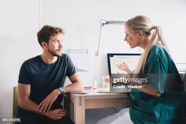 female nurse explaining to young male patient at office in hospital - man in hospital stockfoto's en -beelden