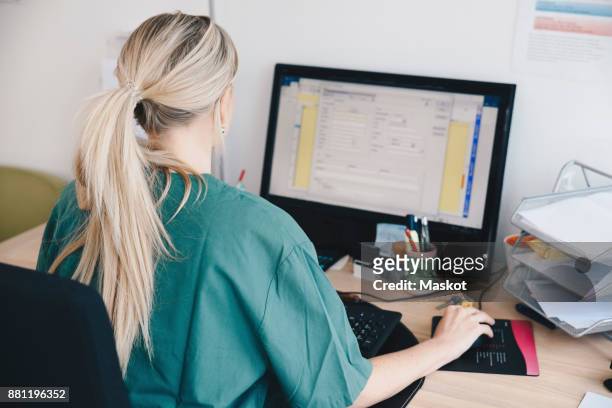 rear view of female nurse working at computer in doctors office - general practitioner stock pictures, royalty-free photos & images