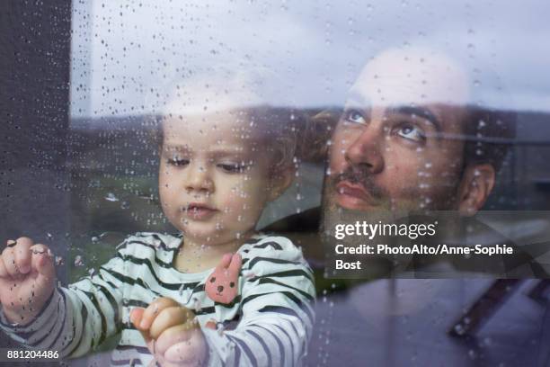 man with young child looking through window watching rain fall - storm photos et images de collection