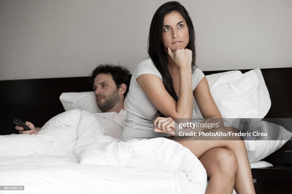 Woman sitting in bed while husband watching tv