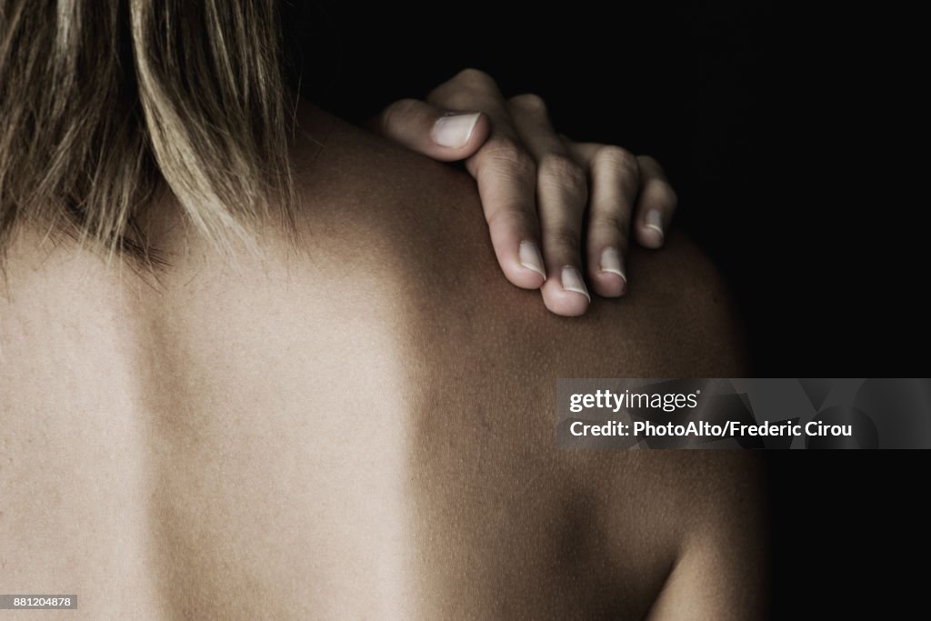 Woman rubbing her bare shoulder, cropped