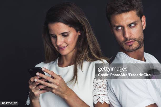 man glaring over his shoulder as girlfriend uses smartphone - sad boyfriend stock pictures, royalty-free photos & images