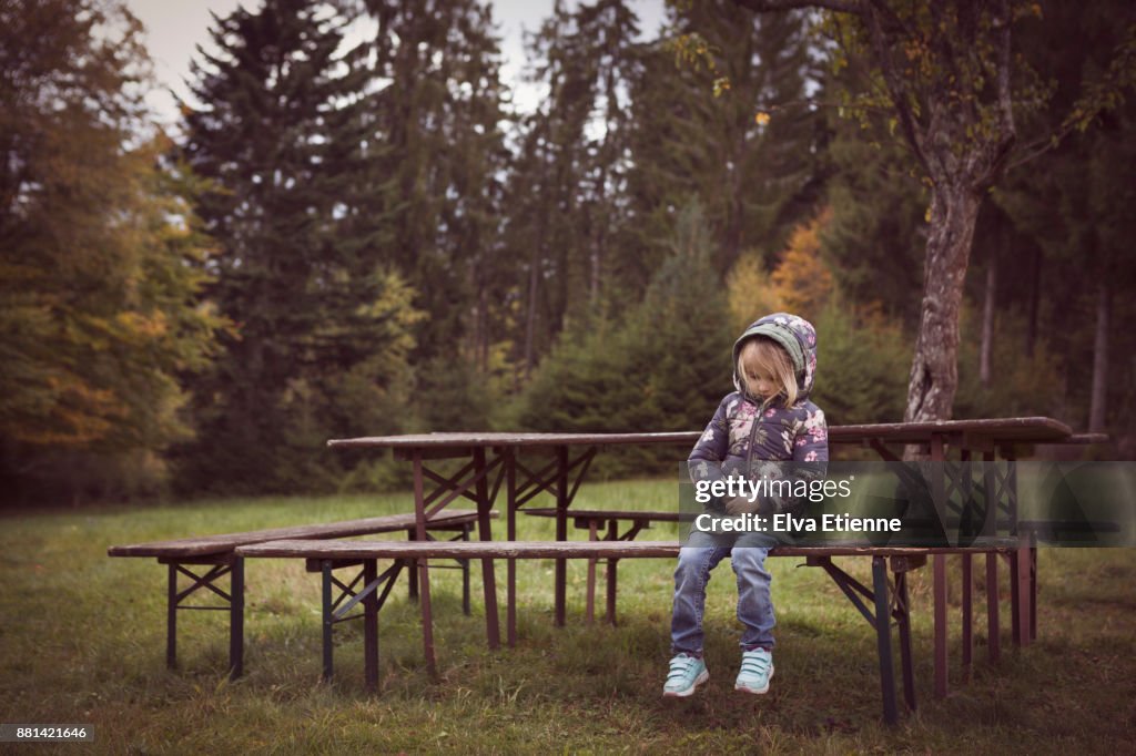 Young, sad child sitting alone at an outdoor picnic table