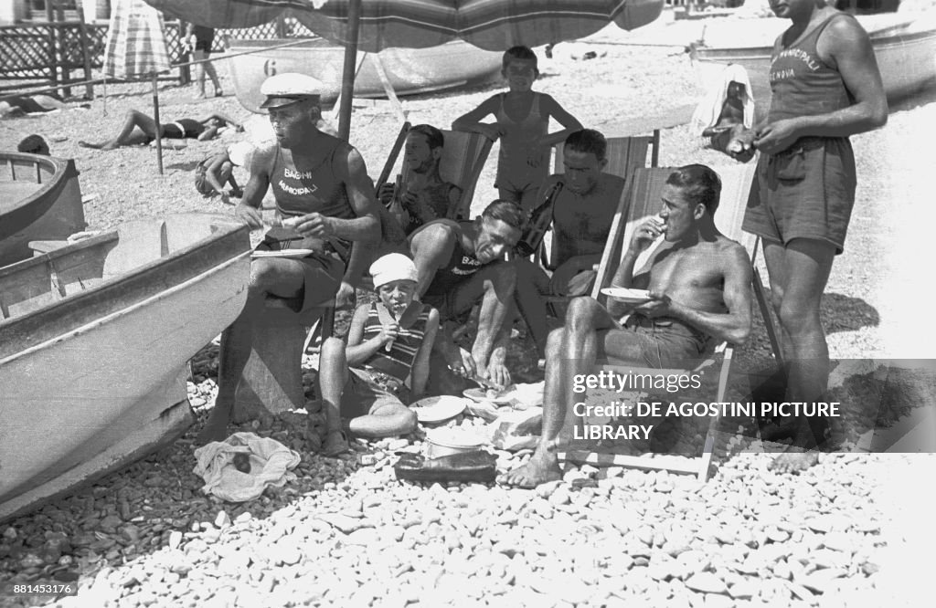 Family on beach eating under parasol, Genoa
