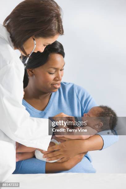 doctor listening to african newborn??s heartbeat - black mother holding newborn stock-fotos und bilder