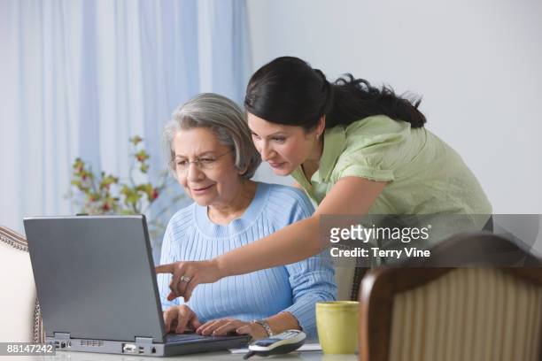 hispanic woman showing senior mother how to use laptop - bill assistance stock pictures, royalty-free photos & images