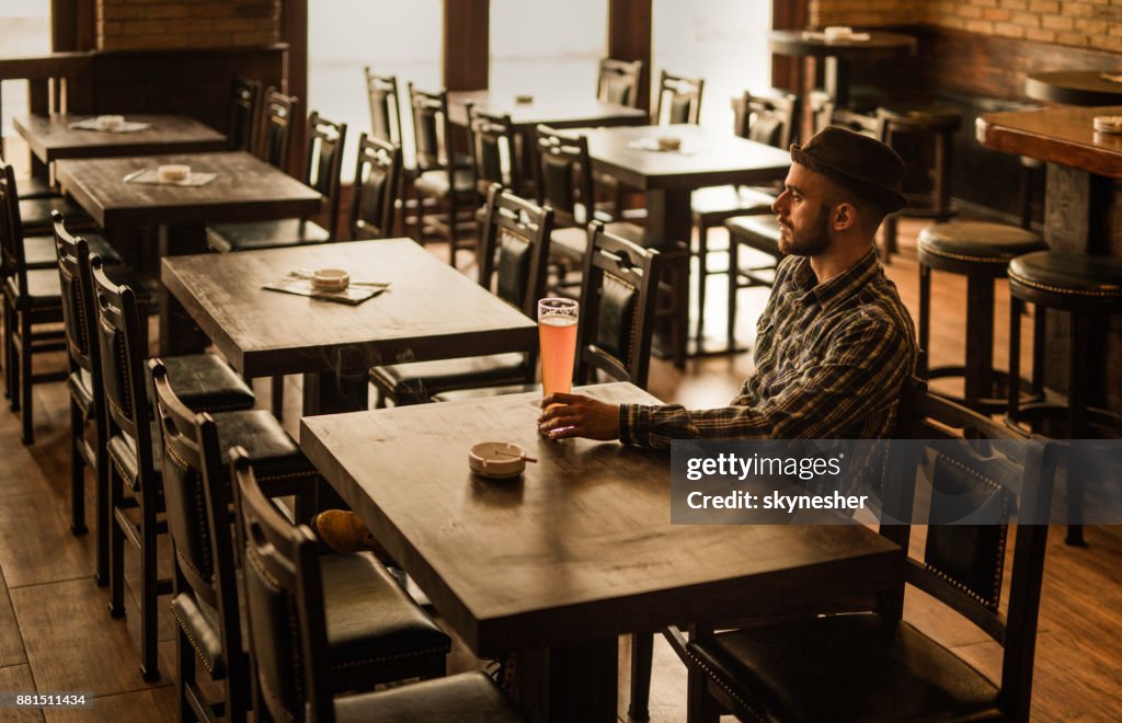 Pensive Man Drinking Beer While Sitting Alone At The Table In
