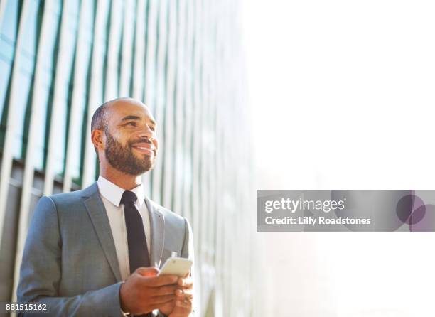 businessman looking up while using mobile phone in modern city environment - dominican ethnicity bildbanksfoton och bilder