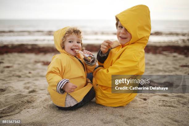 a boy and his little sister on the beach, they wear oilskins - girl oilskin stock pictures, royalty-free photos & images