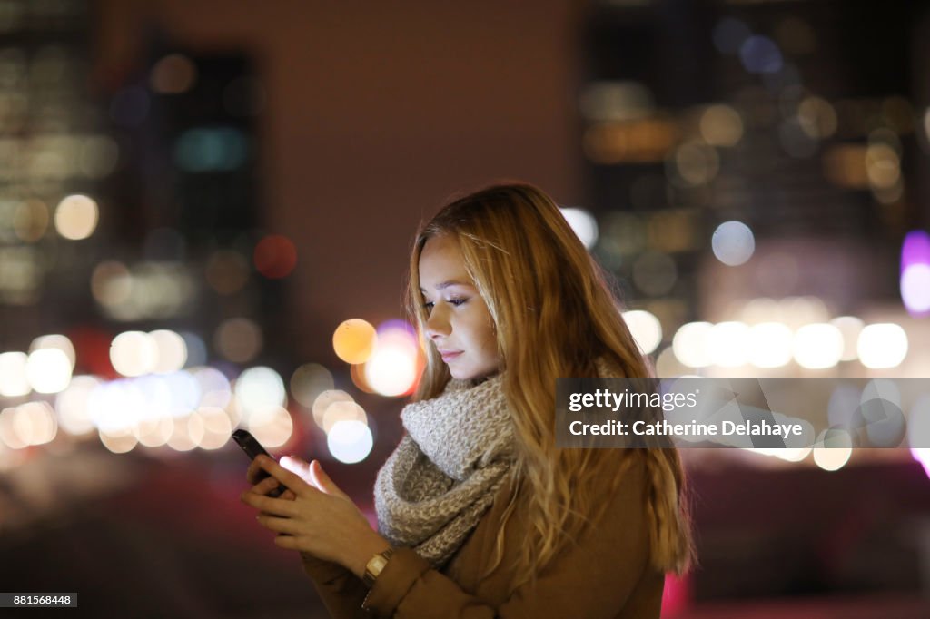 A 17 years old girl with a phone in town by night