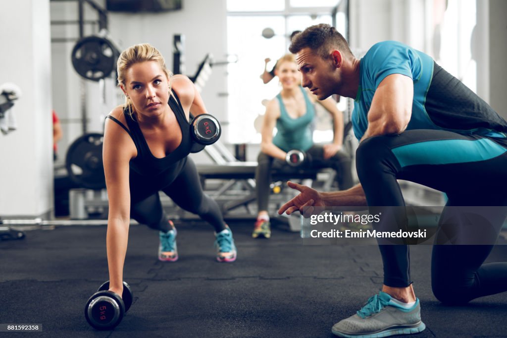 Sporty woman doing push-ups under supervision of personal trainer.