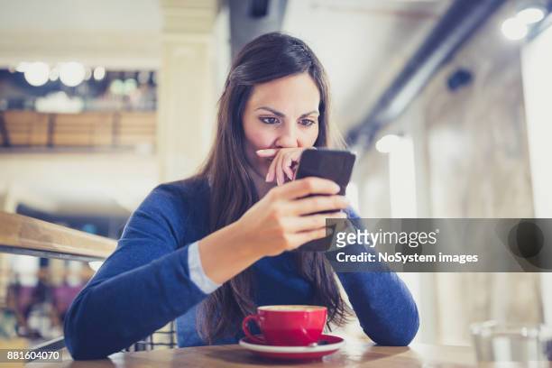 único. mulher jovem preocupada usando telefone inteligente no café - suspicion - fotografias e filmes do acervo