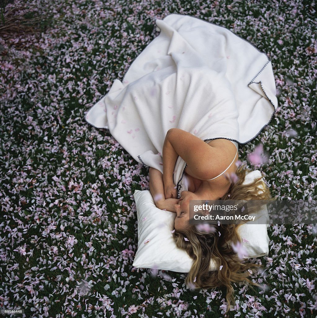 Woman sleeping on grass surrounded by cherry blossom petals