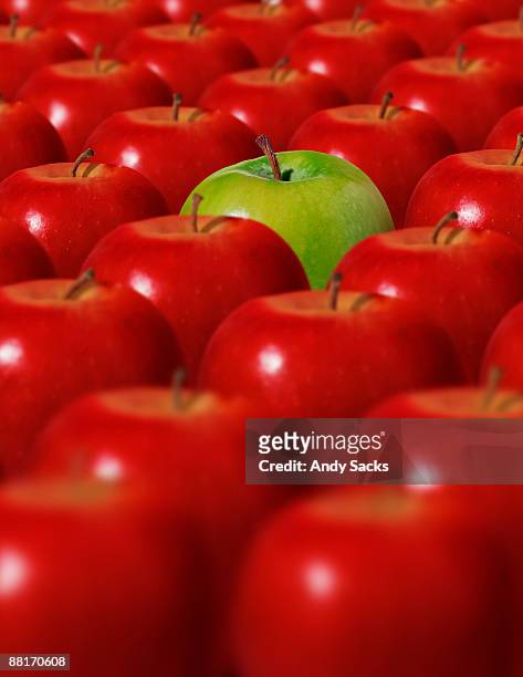 green apple surrounded by red apples - circondare foto e immagini stock