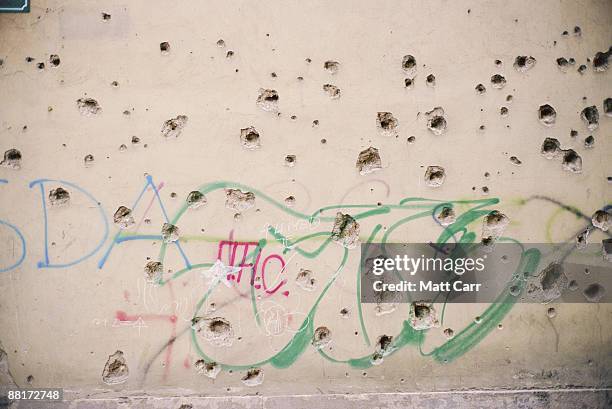 bullet holes in wall with graffiti - bullet holes stock-fotos und bilder