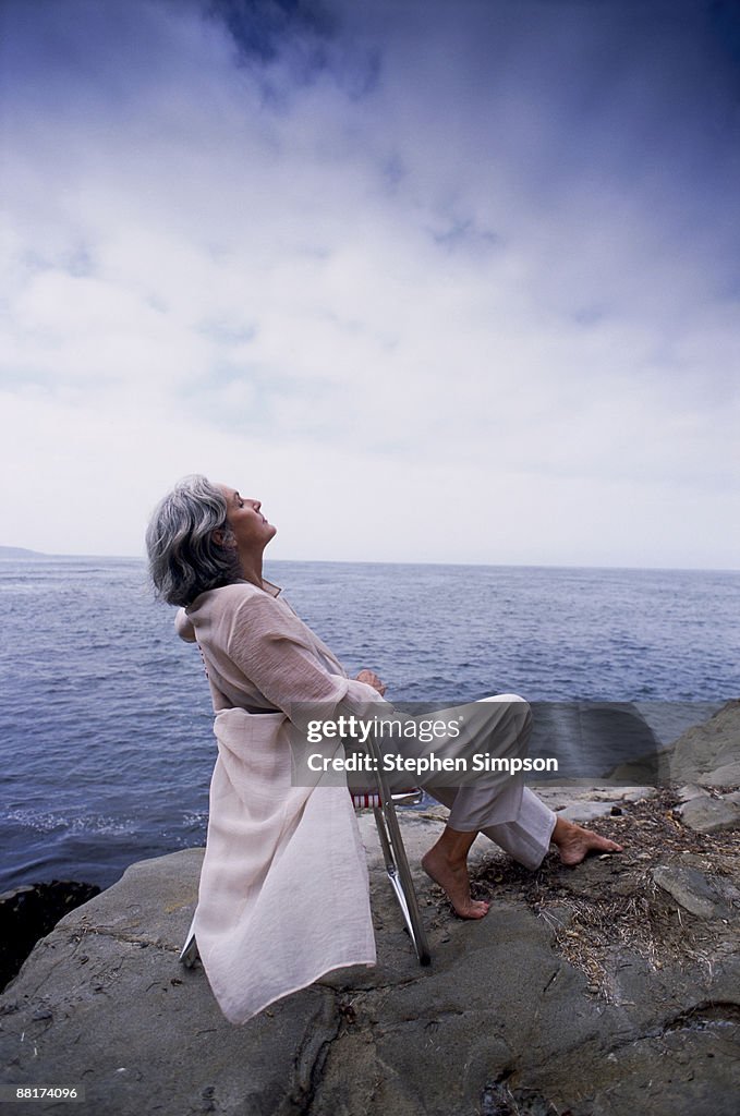 Woman daydreaming on rocky seashore