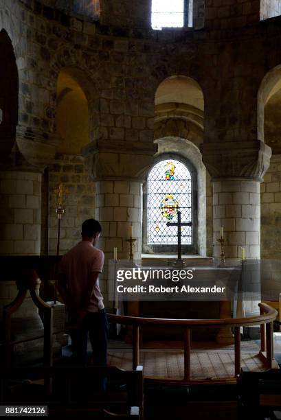 Visitor admires a stained glass window and cross in St. John's Chapel at the Tower of London in London, England. The small chapel is located in White...