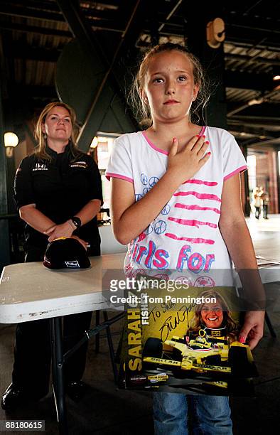 IndyCar driver Sarah Fisher and a young fan stand for the National Anthem while signing autographs for fans before the Oklahoma City RedHawks game at...