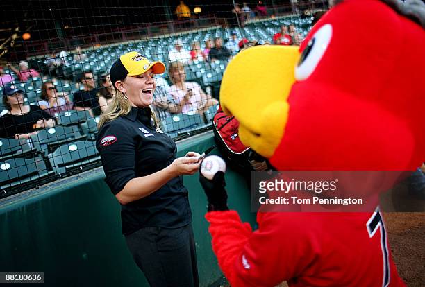 IndyCar driver Sarah Fisher laughs with the RedHawks mascot before throwing out the ceremonial first pitch before the Oklahoma City RedHawks game at...