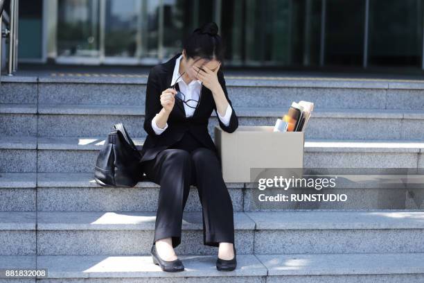 depressed businesswoman sitting on outdoor stairs with packing box - downsizing 2017 film stock-fotos und bilder