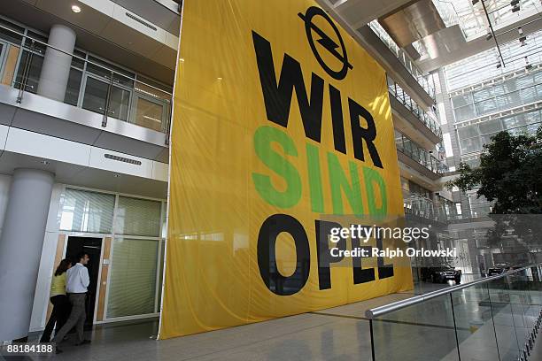 Employees of German car maker Adam Opel GmbH, a subsidiary company of U.S. Carmaker General Motors, walk next a a huge poster at the headquarters...