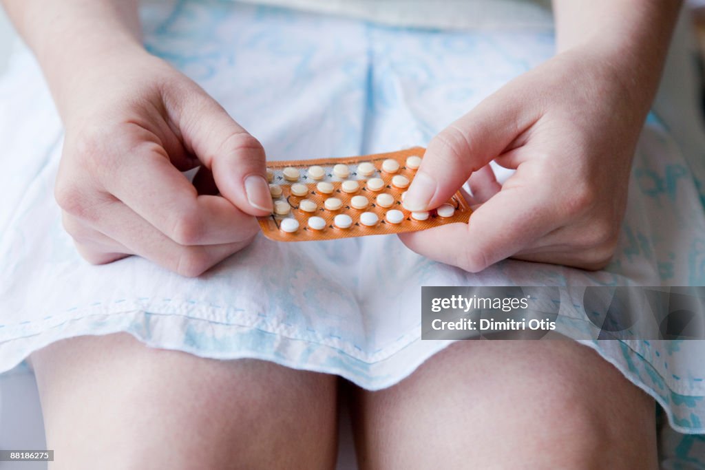 Young woman holding "the pill" on her lap