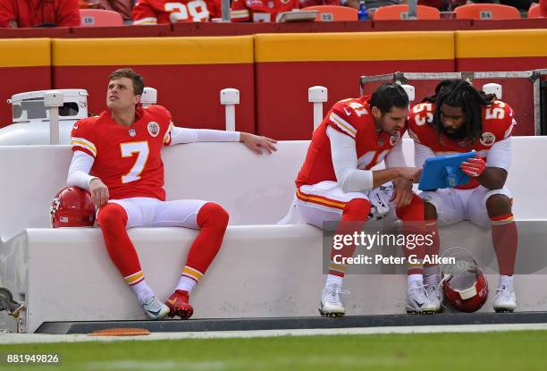 Kicker Harrison Butker of the Kansas City Chiefs looks on from the bench, as teammates James Winchester and Ramik Wilson study a tablet against the...