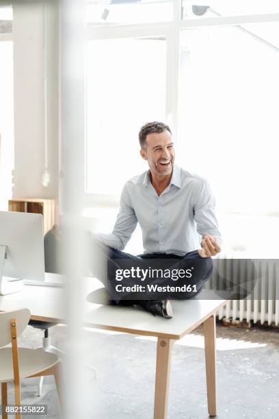 happy businessman sitting on table in office practising yoga - office yoga stock pictures, royalty-free photos & images