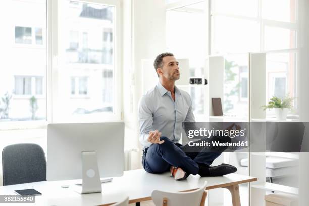 businessman sitting on table in office practising yoga - lotus position stock pictures, royalty-free photos & images