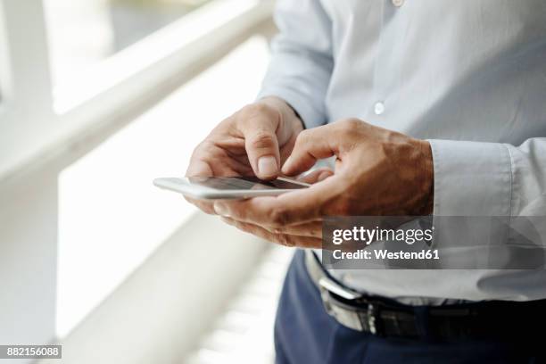 close-up of businessman at the window using cell phone - hand smartphone stock-fotos und bilder